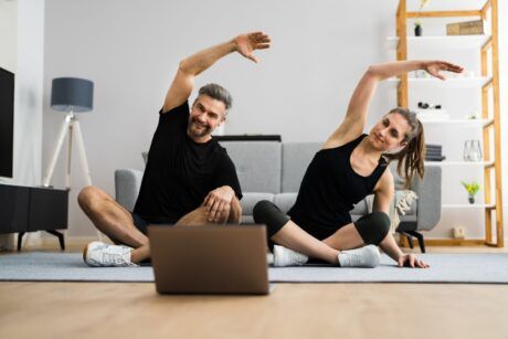 a couple practicing yoga poses in front of a laptop during a 15-minute morning workout session