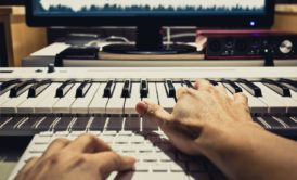 a person plays an electronic keyboard while attending a soundtrack composer masterclass course on a computer