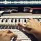 a person plays an electronic keyboard while attending a soundtrack composer masterclass course on a computer