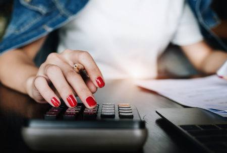 a woman with red nails calculates on a desk, focused on her swing trading course materials