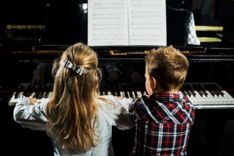 Two children immersed in piano lessons for kids, playing the piano with enthusiasm