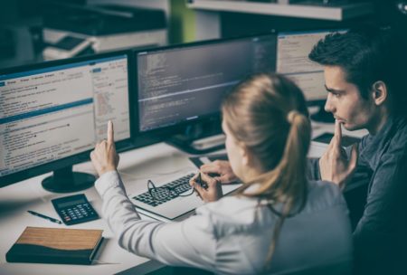 two individuals working on computers in front of a monitor, learning HTML in 1 hour