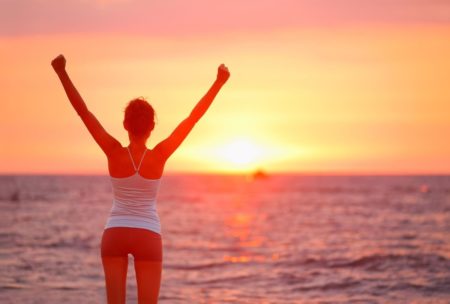 woman raising arms looking at sunset