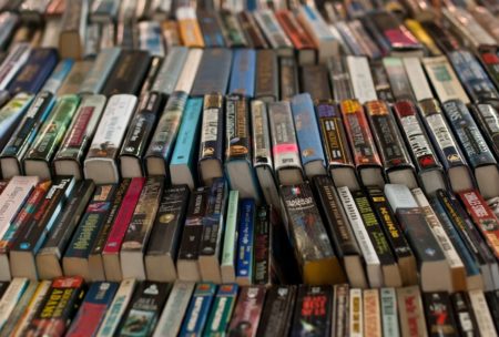 A table stacked with numerous books, primarily fiction writing, forming a substantial pile