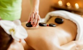 a woman lying face down on a massage table receiving a hot stones massage therapy