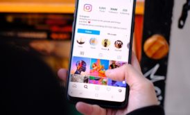 A hand holding a cellphone is scrolling through Instagram after taking an Instagram marketing course