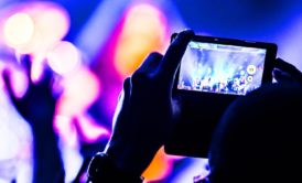 Concertgoer records lively stage performance with vibrant lighting and dynamic musicians during a video and audio production event using their smartphone