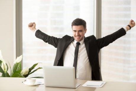 A triumphant man in a suit raises his arms at his desk, symbolizing Motivation Mastery