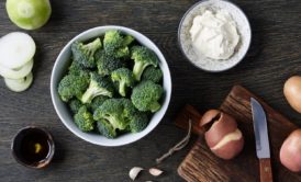 A raw food recipe featuring broccoli, onions, and various ingredients on a wooden table.