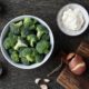 A raw food recipe featuring broccoli, onions, and various ingredients on a wooden table.