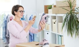 A woman holding shoes while checking her phone, possibly managing her Amazon FBA business