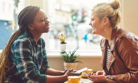 two women sitting at a table, deep in conversation about How To Talk To Anyone