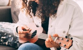 A woman skillfully demonstrates How to Play Ukulele on a cozy couch, showcasing her musical talent and passion