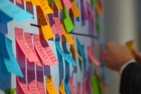 a man in a suit examines a wall covered with colorful post-it notes, reflecting agile scrum user story planning