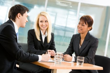 three people wearing suits sitting around a small table and talking to each other