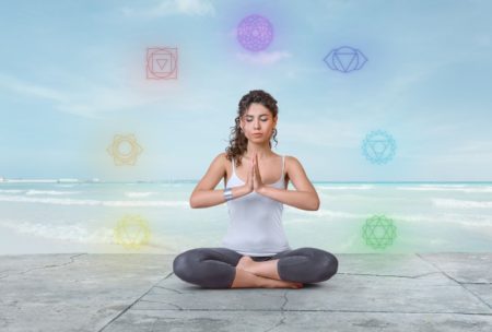 woman in white top and black yoga pants sitting down and meditating on the floor with a psychic course