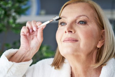 mature woman in white bathrobe putting on makeup