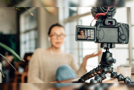 woman wearing light brown sweater recording herself with a camera