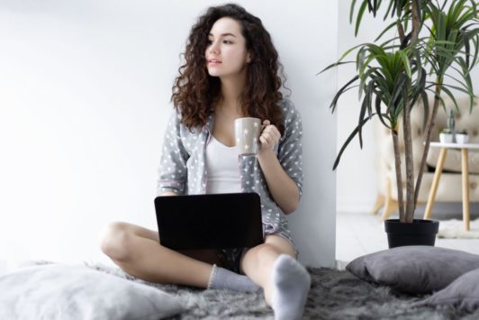 female freelancer holding a cup of coffee and working on laptop