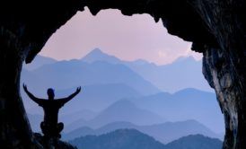 a man stands in a cave with arms outstretched, symbolizing exploration and discovery in a parapsychology course