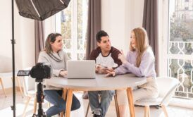 Three people at a table, using a laptop and camera for digital audience engagement.