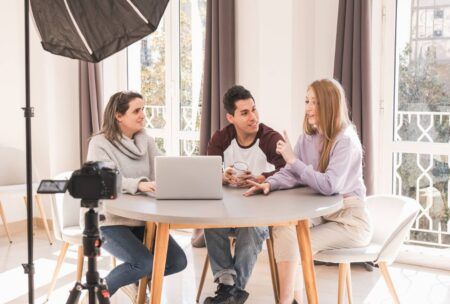 Three people at a table, using a laptop and camera for digital audience engagement.