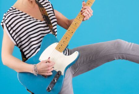 A person in a striped shirt and jeans playing an electric guitar, skillfully mastering guitar chords