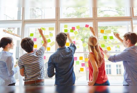 several individuals engaging in team building and problem solving activities by examining sticky notes on a window