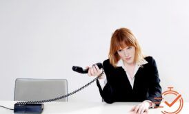 Image of a professional woman at a desk with a phone and a 10 minutes sign, handling abusive customers.