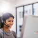 Woman wearing headset smiles at computer, delivering advanced customer service.