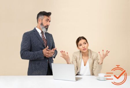 Two professionals in business clothes are seated at a table with a laptop, focused on a course about managing difficult customers.