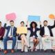 Business professionals sitting on chairs with speech bubbles, discussing how to improve employee engagement.