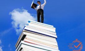 A man stands triumphantly on a pile of books, symbolizing the wisdom and knowledge needed to succeed in business.