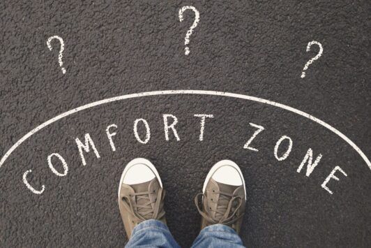 feet standing on road with question marks and comfort zone sign, symbolizing leaving the comfort zone