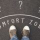 feet standing on road with question marks and comfort zone sign, symbolizing leaving the comfort zone