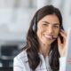 a smiling woman wearing a headset operates a computer, actively participating in outbound calling