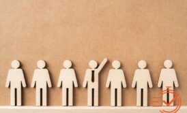 Wooden figures gather in front of a brown wall, representing collaboration and taking initiative in a workplace setting.