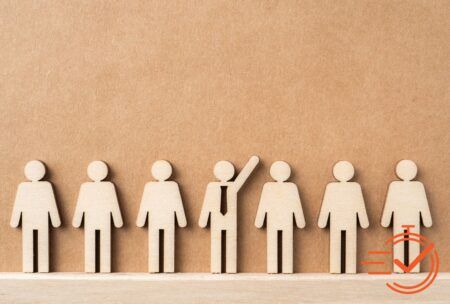 Wooden figures gather in front of a brown wall, representing collaboration and taking initiative in a workplace setting.