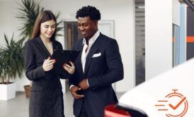 a man and woman at a car dealership, focused on a tablet, exploring options with a customer first approach