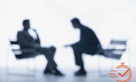 Two people seated in chairs, discussing interviewing skills for interviewers against a clean white backdrop