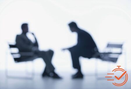 Two people seated in chairs, discussing interviewing skills for interviewers against a clean white backdrop