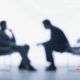 Two people seated in chairs, discussing interviewing skills for interviewers against a clean white backdrop