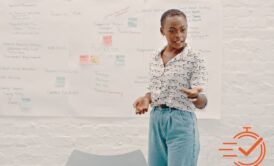 A woman stands confidently in front of a whiteboard, leading a presentation skills training session.