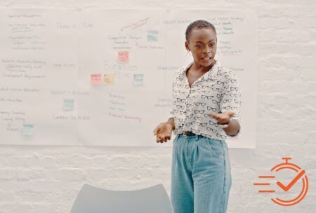 A woman stands confidently in front of a whiteboard, leading a presentation skills training session.