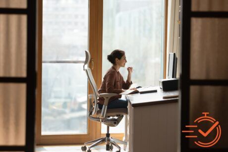 A woman at an ergonomic home office desk, focused, with a window view brightening her workspace.