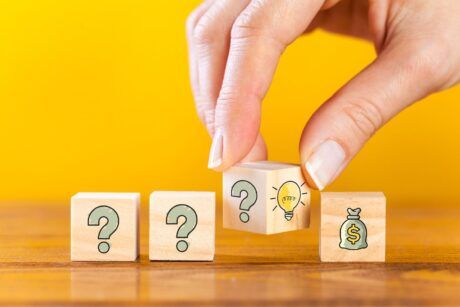 Wooden blocks with a question mark and money symbol are held by a hand, illustrating the problem-solving process