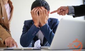 A man sits at a laptop, holding his head in frustration, symbolizing the struggle with workplace bullying.