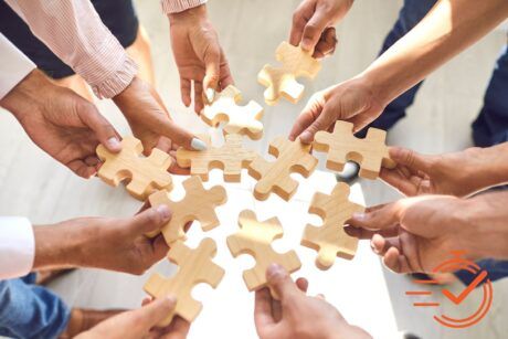 A group of people, holding wooden puzzle pieces, symbolizing collaboration during a corporate teamwork activity.