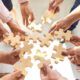 A group of people, holding wooden puzzle pieces, symbolizing collaboration during a corporate teamwork activity.