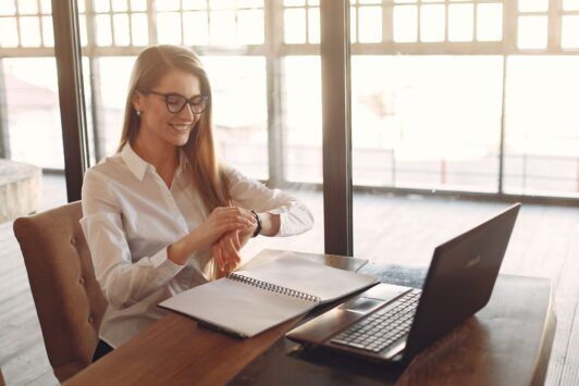 a woman with glasses at a table uses her laptop, concentrating on strategies on how to build self discipline